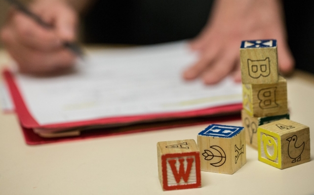 Wooden blocks with letters, numbers and pictures on the side, stacked in front of a folder that someone is writing on